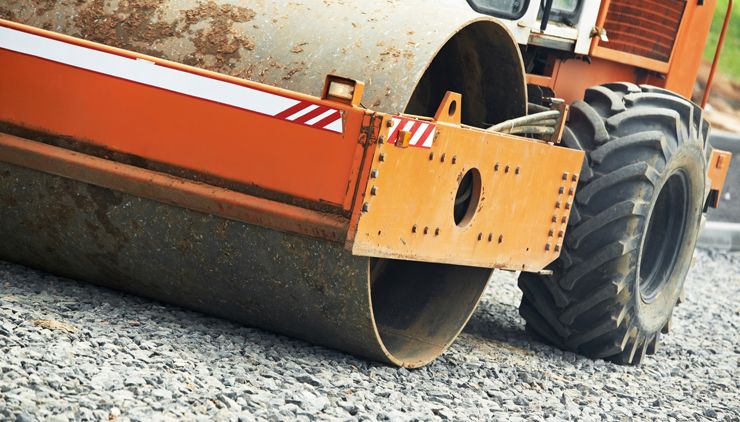 Tractor rolling farm roadway crushed stone.