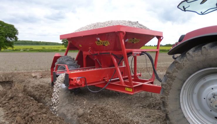 Tractor spreading drainage stone on land.